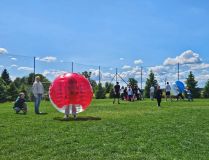 Uczniowie bawią się w bomber ball – dynamiczna scena na trawie, piłki z uczniami w środku, uczniowie w ruchu.