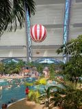 Widok wnętrza Tropical Islands – palmy, duży basen,  ludzie w strojach kąpielowych. Duży balon nad basenem.