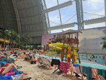 Widok wnętrza Tropical Islands – palmy, duży basen, zjeżdżalnie i dzieci w strojach kąpielowych. 