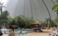 Widok wnętrza Tropical Islands – palmy, duży basen, plaża, trzcinowe domki.
