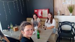 Uczennice klasy 5 c w lokalu pizzerii  ,,105” siedzą przy stoliku i uśmiechają się do zdjęcia.