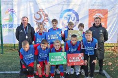 Na tle białego baneru z  logo organizatora i sponsorów turnieju stoi dziewięcioosobowa reprezentacja szkoły chłopców w roczniku 2012 wraz z trenerem Michałem Lubińskim i przedstawicielem PZPN.