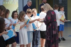 Uczniowie klasy 3b otrzymują na forum szkoły pamiątkowe książki i dyplomy z okazji ukończenia pierwszego etapu edukacyjnego.