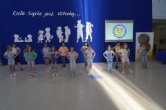 Członkinie szkolnego zespołu tanecznego ubrane w dżinsowe ogrodniczki prezentują układ taneczny na forum szkoły.