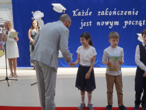 Na tle okolicznościowej dekoracji widać Laureatów Ogólnopolskiej Olimpiady Przedmiotowej Olimpusek. Nagrody wręcza Przewodniczący Rady Rodziców- Pan Przemysław Zieliński. Na drugim planie, przy mikrofonie, stoi Pani Agnieszka Jaroszewska – koordynator konkursu.