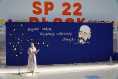 Na tle okolicznościowej dekoracji, przedstawiającej rysunek twarzy patrona Szkoły- Janusza Korczaka oraz zapis fragmentu jego myśli „Bądź sobą. Szukaj własnej drogi...” widać p. Natalię Szwech- konferansjera uroczystości zakończenia roku szkolnego klas trzecich.