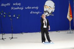 Na scenie stoi solistka chóru szkolnego Tu Tu i śpiewa piosenkę.