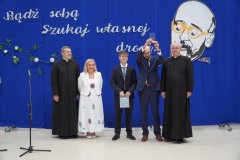 Na scenie stoi nagrodzony medalem Janusza Korczaka – Absolwent klasy 8b w towarzystwie Pani Dyrektor, Księży parafii św. Wojciecha i Przewodniczącego Rady Rodziców