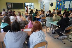 Sala chemiczna, uczestnicy konkursu podzieleni na 3-4 osobowe grupy siedzą przy ławkach, wita ich nauczycleka fizyki, p. Celina Krysińska, w tle slajd przeentacji multimedialnej z wizerunkiem uczonej oraz napis "Spotkanie z Marią Skłodowską-Curie 7 listopada 2024".