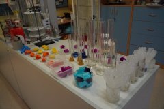 Dygestorium w sali chemicznej z przygotowanymi do doświadczenia "tęcza w probówce": cylindrami miarowymi, pipetami, naczyniami z paskami kolorowej bibuły do barwienia wody itp.