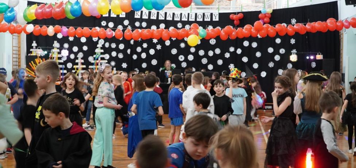 Tańczący uczniowie wśród balonów na sali gimnastycznej.
