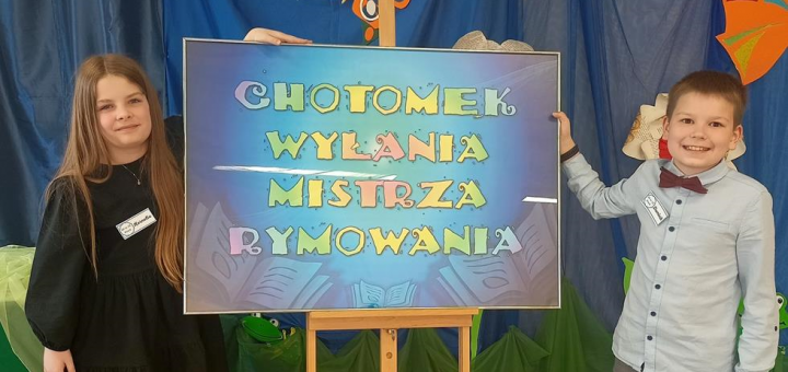 Dwoje uczniów z naszej szkoły – Kornelia i Dominik pozują przy kolorowej planszy „Chotomek” wyłania Mistrza Rymowania.