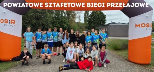Zdjęcie reprezentacji Szkoły Podstawowej nr 22 w Płocku na Powiatowych Sztafetowych Biegach Przełajowych - grupa dziewcząt i chłopców w niebieskich strojach sportowych pozująca pod pomarańczowo – białą – czarną bramą MOSiR Płock. Na górze napis: Powiatowe sztafetowe biegi przełajowe