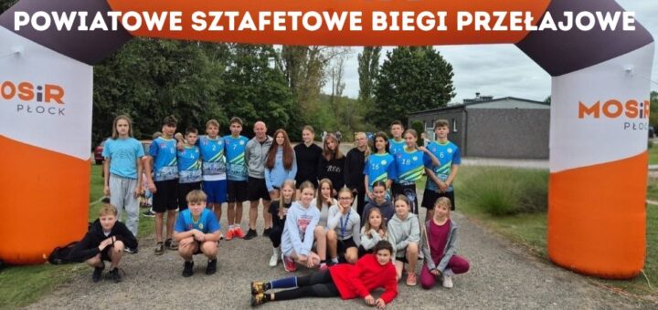 Zdjęcie reprezentacji Szkoły Podstawowej nr 22 w Płocku na Powiatowych Sztafetowych Biegach Przełajowych - grupa dziewcząt i chłopców w niebieskich strojach sportowych pozująca pod pomarańczowo – białą – czarną bramą MOSiR Płock. Na górze napis: Powiatowe sztafetowe biegi przełajowe